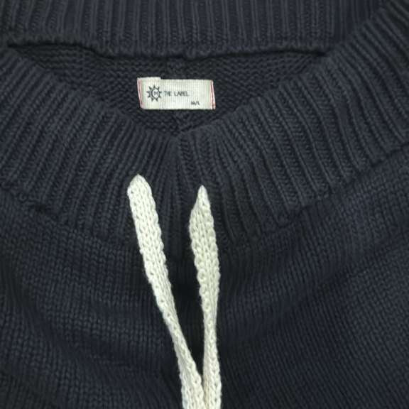 Black knitted sweater pant waisteband with a brand label on a dark background