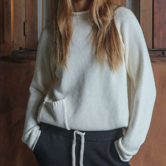 Person wearing a white knitted sweater and dark knitted pants with white drawstring in a wooden interior 